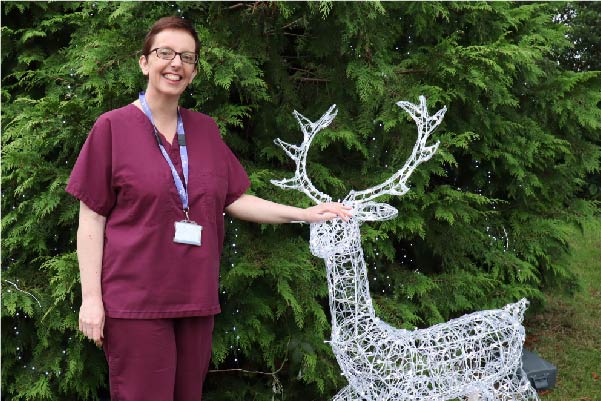 Hospice nurse standing next to a Christmas tree with a light up Reindeer
