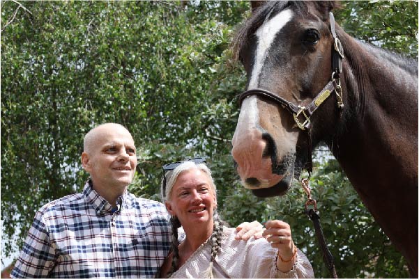 Shaun and his wife smiling next to a shire horse