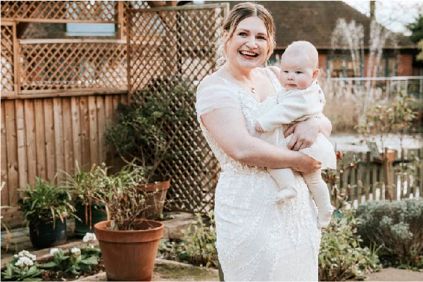 Lucy holding her baby Everlie wearing a wedding gown in the St Helena Hospice gardens
