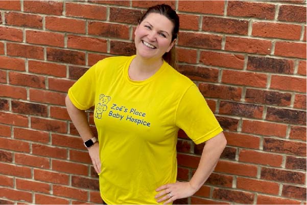 Rachel wearing a bright yellow Zoe's Place Baby Hospice t-shirt smiling