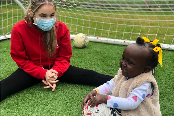 Children's hospice nurse sitting on a field with small child